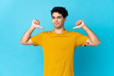 Genç Venezuelalı adam mavi arka planda soyutlanmış gururlu ve kendinden memnun