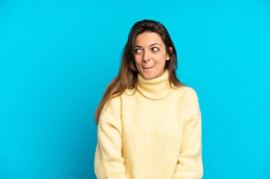 Kafkasyalı genç bir kadın mavi arka planda izole edilmiş, yukarı bakarken şüpheleri var.