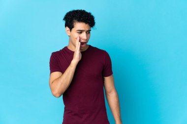 Genç Venezuelalı bir adam mavi arka planda izole edilmiş. Yan tarafa bakarken sürpriz bir jest yapıyor.