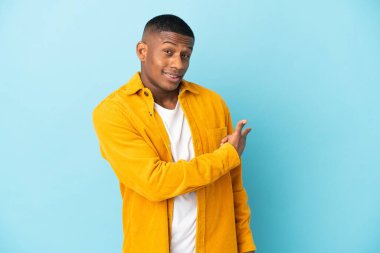 Mavi arka planda izole genç latin adam geriye işaret ediyor