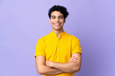 Genç Venezuelalı adam mor arka planda izole edilmiş, kollarını ön konumda tutuyor.