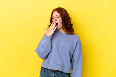 Teenager reddish woman isolated on yellow background yawning and covering wide open mouth with hand