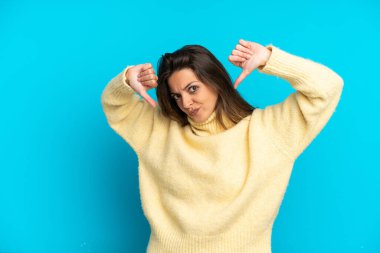 Mavi arka planda izole edilmiş beyaz bir kadın baş parmağını iki eliyle aşağı gösteriyor.