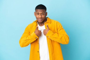 Mavi arka planda yalıtılmış genç latin adam, şaşırmış yüz ifadesi ile