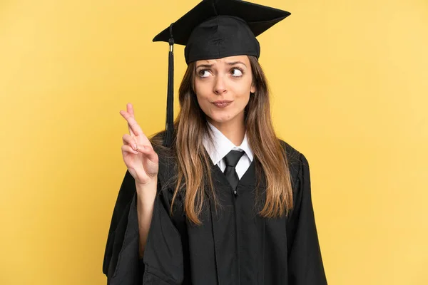 Young University Graduate Isolated Yellow Background Fingers Crossing Wishing Best — ストック写真