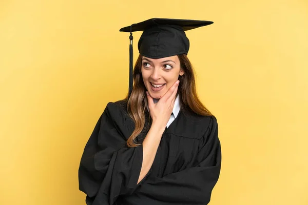 Junger Universitätsabsolvent Isoliert Auf Gelbem Hintergrund Und Lächelnd Aufblickend — Stockfoto