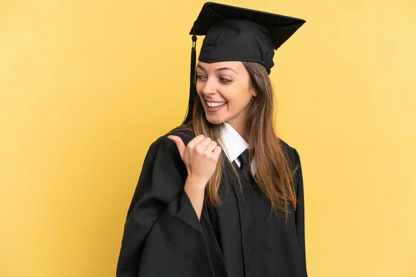 製品を提示する側を指す黄色の背景に隔離された若い大学の卒業生 — ストック写真