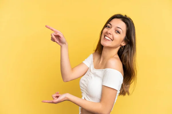 黄色の背景に指を向け製品を提示する若い白人女性 — ストック写真