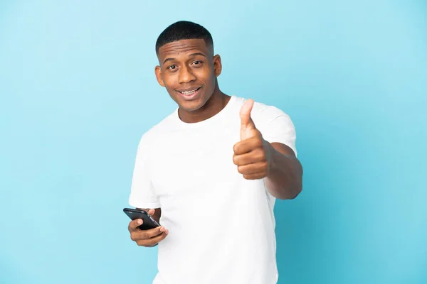 Jovem Latino Isolado Fundo Azul Usando Telefone Celular Enquanto Fazendo — Fotografia de Stock