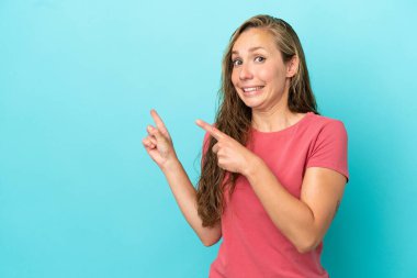 Mavi arka planda izole edilmiş genç beyaz kadın korkmuş ve kenarı işaret ediyor.