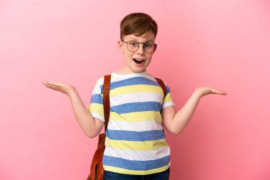 Küçük kızıl saçlı beyaz çocuk pembe arka planda izole edilmiş, şok olmuş bir yüz ifadesi var.