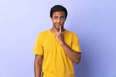 Örgülü genç Afrikalı Amerikalı adam mor arka planda izole edilmiş ve düşünüyor.