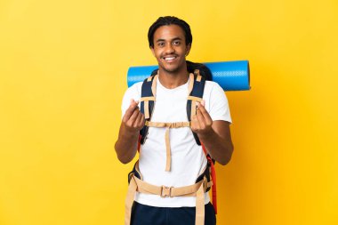 Sarı arka planda büyük bir sırt çantalı genç dağcı para hareketi yapıyor.