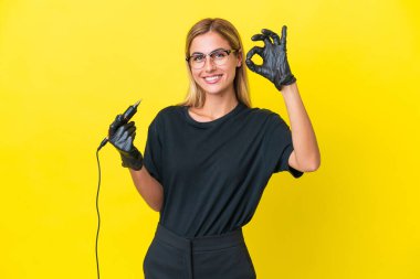 Dövme sanatçısı Uruguaylı kadın sarı arkaplanda izole edilmiş ve parmaklarıyla işaret gösteriyor