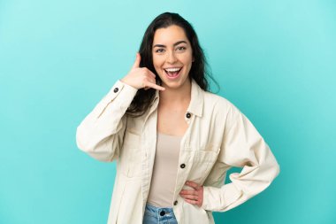 Mavi arka planda izole edilmiş beyaz bir kadın telefon jesti yapıyor. Bana geri dönüş işareti ver.