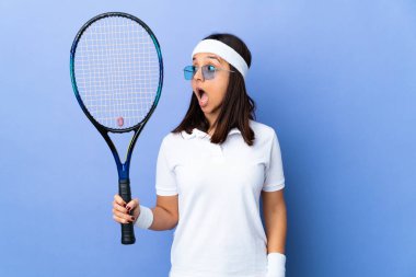 İzole edilmiş arka planda genç bayan tenisçi yan tarafa bakarken sürpriz jest yapıyor.