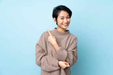 Tecrit edilmiş arka planda kısa saçlı genç Vietnamlı kadın bir ürünü sunmak için kenarı işaret ediyor.