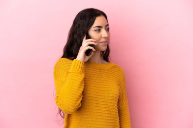 Pembe arka planda izole edilmiş cep telefonu kullanan beyaz bir kadın yan tarafa bakıyor.