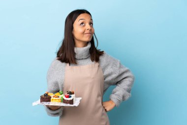 Pasta şefi elinde büyük bir pasta tutarak izole edilmiş mavi arkaplanı inceliyor..