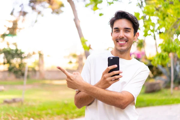 Jovem Caucasiano Parque Usando Telefone Celular Apontando Para Trás — Fotografia de Stock