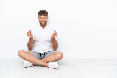 Yerde yatan genç sarışın adam beyaz arka planda izole bir şekilde para hareketi yapıyor.