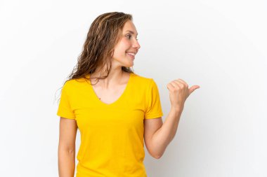 Beyaz arka planda izole edilmiş genç beyaz kadın bir ürünü sunmak için kenarı işaret ediyor.