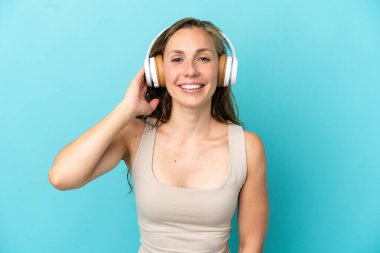Genç beyaz kadın mavi arka planda izole edilmiş müzik dinliyor.