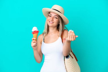 Elinde dondurma ve plaj çantası olan genç Romen kadın mavi arka planda izole edilmiş bir şekilde el ele gelmeye davet ediliyor. Gelmene sevindim.