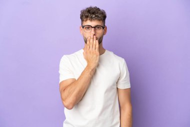 Teslimat yapan beyaz adam, mor arka planda izole edilmiş, ağzı elle kapatılmış.