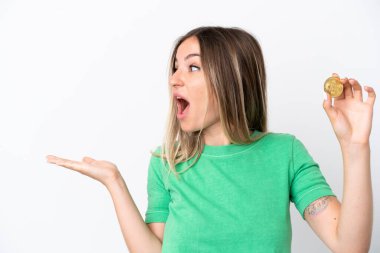 Beyaz arka planda yüzü sürpriz bir ifadeyle izole edilmiş bir Bitcoin tutan genç Romen kadını