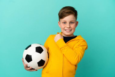 Mavi arka planda futbol oynayan kızıl saçlı çocuk zaferi kutluyor.