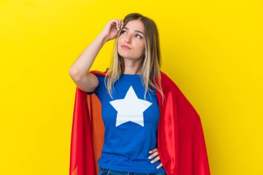 Süper Kahraman Rumen kadın sarı arka planda izole edilmiş şüpheleri ve kafa karıştırıcı yüz ifadesiyle