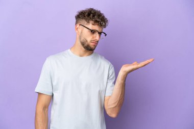 Mor arka planda izole edilmiş beyaz bir adam. Kopyalama alanını şüphe ile tutuyor.