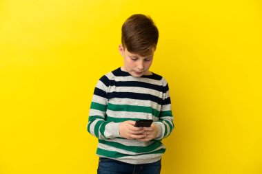 Sarı arka planda izole edilmiş küçük kızıl çocuk cep telefonuyla mesaj yolluyor.