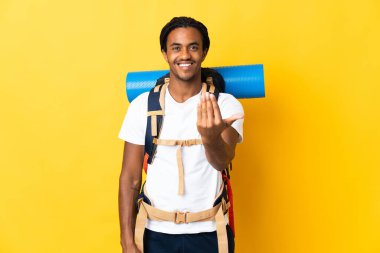 Sarı arka planda izole edilmiş büyük bir sırt çantalı genç dağcı, elini uzatmaya davet ediyor. Gelmene sevindim.