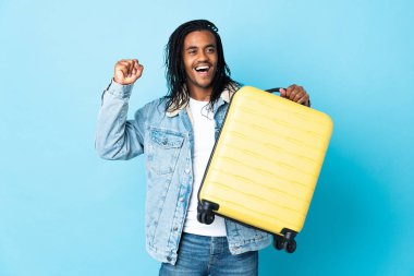 Mavi arka planda saç örgüleri olan genç Afrikalı Amerikalı bir adam seyahat çantasıyla tatilde.