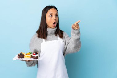 Pasta şefi izole edilmiş mavi arka planda büyük bir pasta tutuyor..