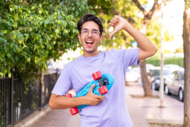 Parkta yüzünde mutlu bir ifadeyle paten yapan beyaz bir genç.