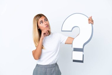 Sarışın Uruguaylı kız beyaz arka planda izole edilmiş elinde bir soru işareti simgesi var ve şüpheleri var.