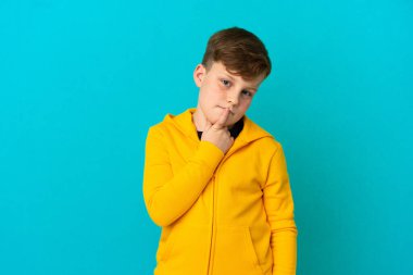 Mavi arka planda izole edilmiş küçük kızıl saçlı çocuk yukarı bakarken şüpheleri var.