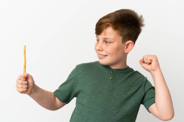 Beyaz arka planda izole edilmiş diş fırçası tutan kızıl saçlı çocuk zaferi kutluyor.