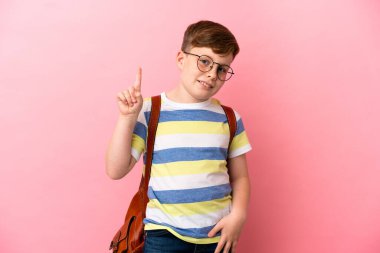 Pembe arka planda izole edilmiş küçük kızıl saçlı çocuk harika bir fikre işaret ediyor.