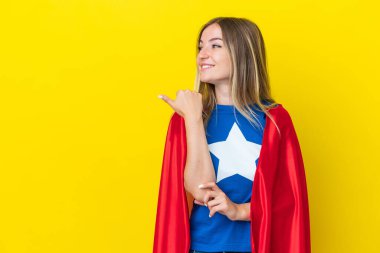 Süper Kahraman Rumen kadın, sarı arka planda izole edilmiş bir şekilde bir ürün sunmak için kenarı işaret ediyor