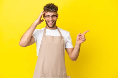 Restoran garsonu. Sarı arka planda izole edilmiş sarışın adam. Şaşırmış ve işaret ediyor.
