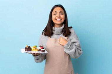 Pasta şefi mavi arka planda büyük bir pasta tutuyor ve gülüyor..