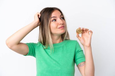 Beyaz arka planda izole edilmiş bir Bitcoin tutan genç Romen kadının şüpheleri ve kafa karıştırıcı yüz ifadesi var