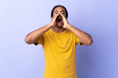 Örgülü genç Afrikalı Amerikalı adam mor arka planda izole edilmiş bağırıyor ve bir şey duyuruyor.