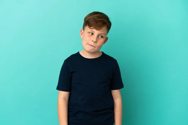 Pequeño Pelirrojo Aislado Sobre Fondo Azul Teniendo Dudas Mientras Mira —  Fotos de Stock