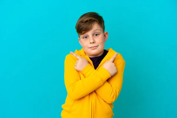 Kleine Roodharige Jongen Geïsoleerd Blauwe Achtergrond Wijzend Naar Lateralen Met — Stockfoto