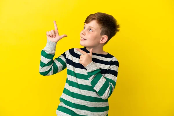 红头发的小男孩被黄色的背景隔离了 用食指指尖着是个好主意 — 图库照片
